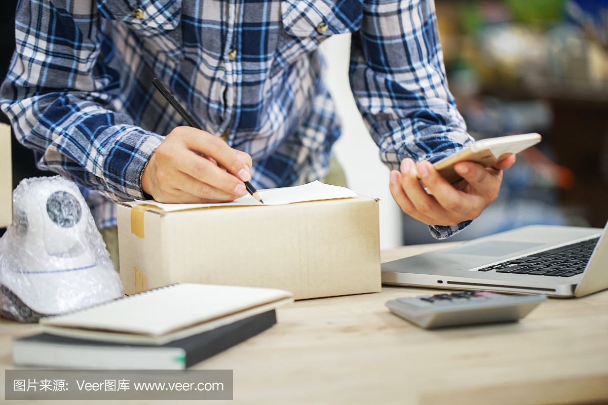 年輕的創業小企業主在工作場所的盒子里裝攝像頭閉路電視。自由職業者銷售者準備產品的包裝過程在家里。網絡銷售,網絡營銷,